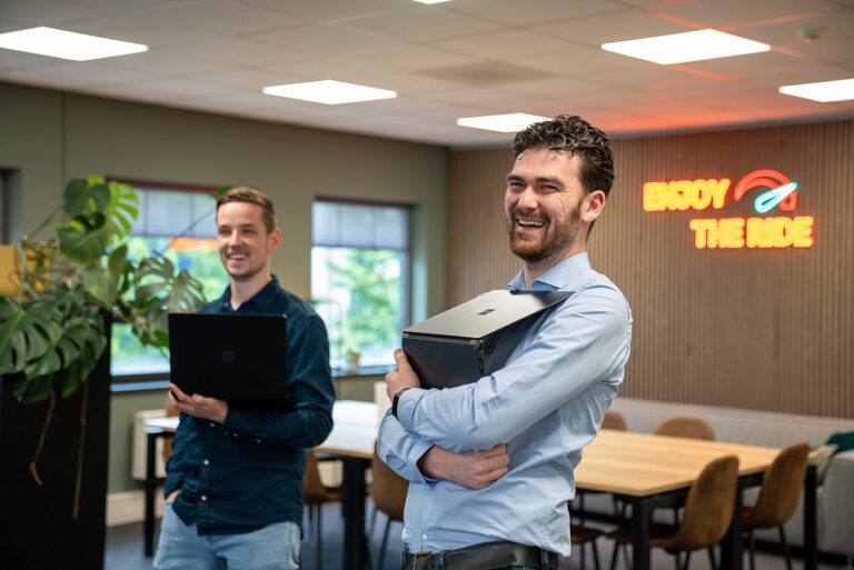 Twee lachende mannen staan in het kantoor met laptops in hun handen