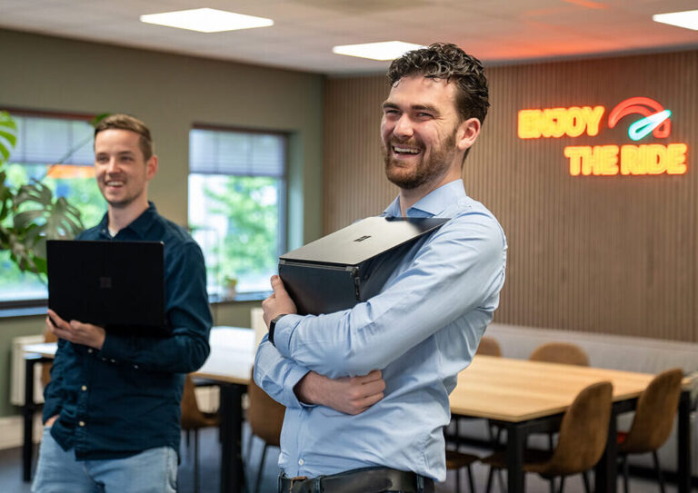 Twee lachende mannen staan in het kantoor met laptops in hun handen
